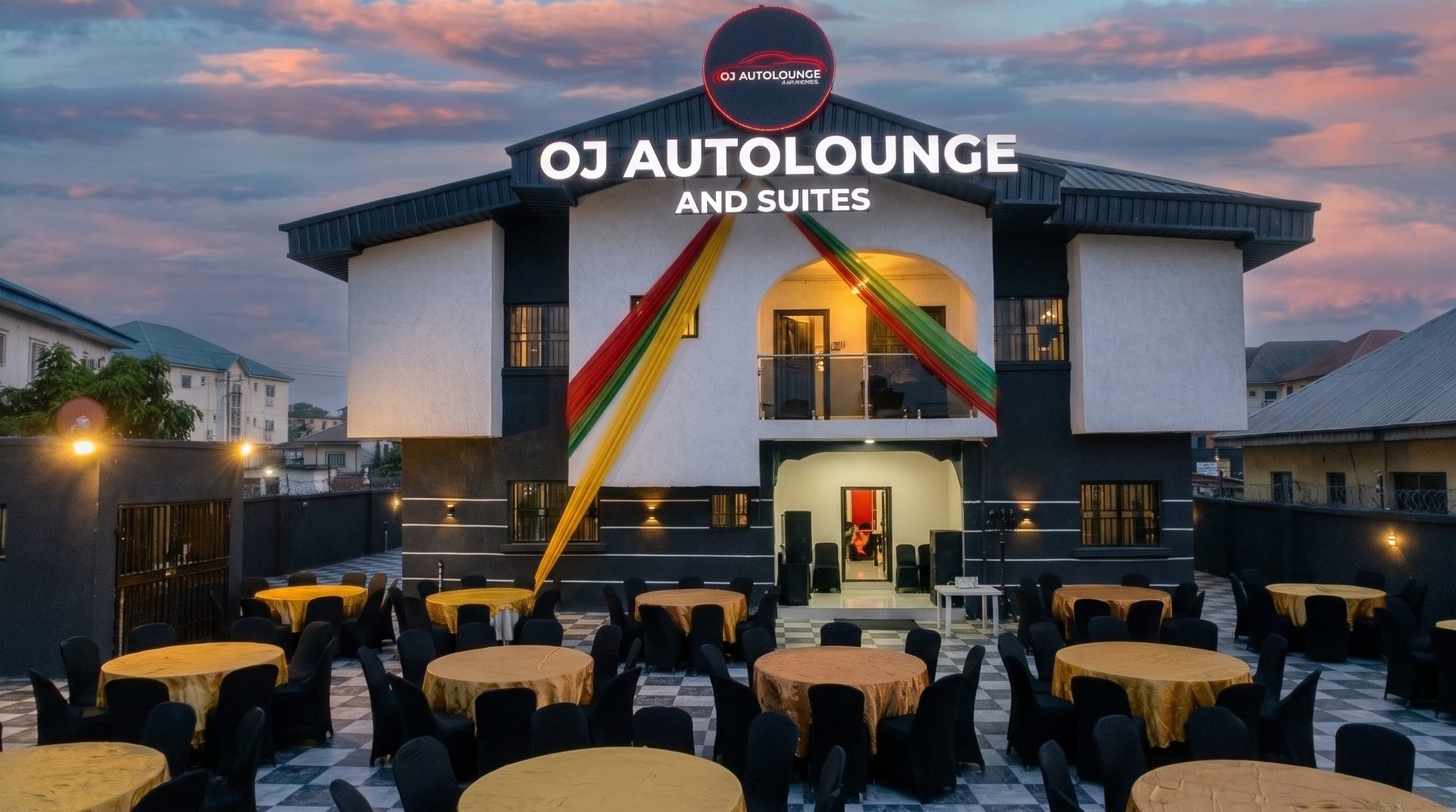 OJAUTOLOUNGE AND SUITE at dusk: lit sign, coloured ribbons on the facade and a checkerboard courtyard set with tables
