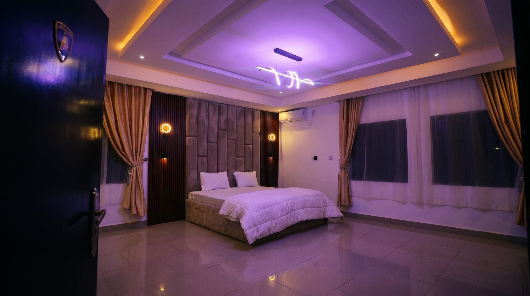 The Lamborghini suite: bedroom with purple ceiling light, seen past the door with the Lamborghini badge
